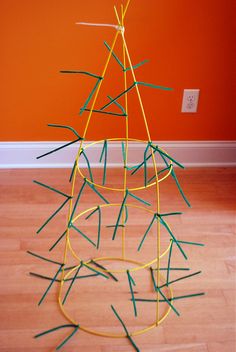 a sculpture made out of sticks on top of a hard wood floor next to an orange wall