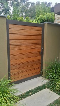 a large wooden door in the side of a house with grass and bushes around it