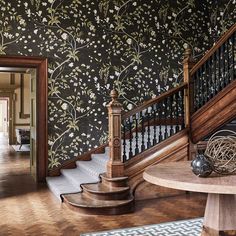 an ornate staircase with floral wallpaper on the walls and wooden handrails, along with a round coffee table