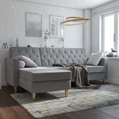 a living room with white brick walls and wooden floors, a gray sectional sofa is next to a rug on the floor