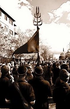 a crowd of people standing around each other in front of a tall building with a flag on it