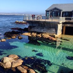 people are standing on the pier looking out at the water and rocks in front of them