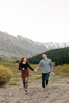 a man and woman holding hands while walking in the mountains