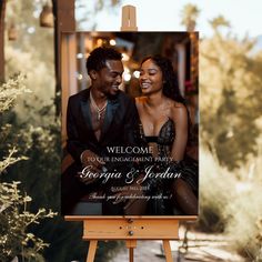 an easel with a welcome sign and a photo of a couple on it in front of some bushes