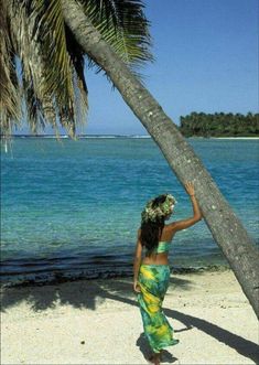 a woman standing on top of a sandy beach under a palm tree next to the ocean