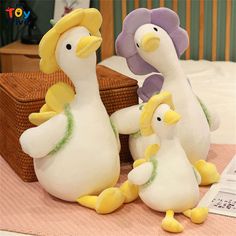 three stuffed ducks sitting on top of a bed next to a basket filled with toys