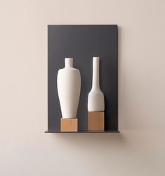 two white vases sitting on top of a wooden shelf next to a gray wall