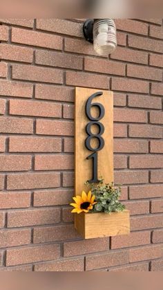 a house number sign mounted to the side of a brick wall with a sunflower