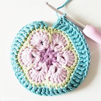 a crocheted pot holder with a pink and blue flower on it next to a knitting needle