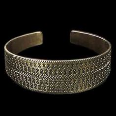 a silver bracelet with an intricate design on the front and back side, against a black background