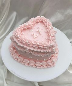 a heart shaped cake with pink frosting and pearls on top sits on a white plate