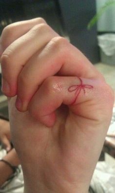 a person's hand with a small red spider tattoo on their left index finger