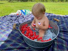 a baby sitting in a metal tub filled with cherries on top of a blanket