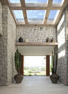 the inside of a house with stone walls and large cactus pots on either side of the entrance