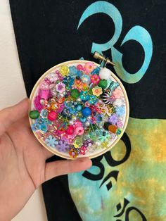 a hand holding a needle case filled with lots of different colored beads and charms on it