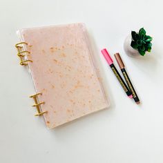 a notebook, pen and plant on a white surface