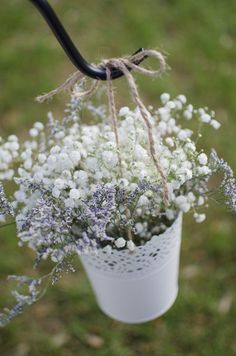 a white bucket filled with lots of flowers hanging from a metal hook in the grass