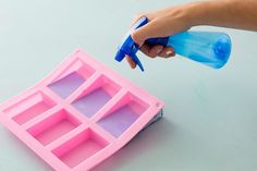 a hand holding a blue plastic bottle over a pink ice cube tray with holes in it