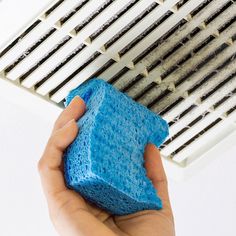 a person holding a blue sponge in front of an air conditioner and ventilator