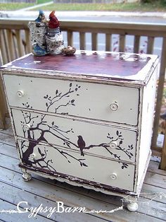 an old dresser has birds painted on it and is sitting on a deck with other items