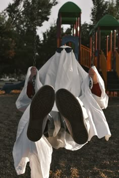 a person sitting on a swing with their feet in the air while wearing white clothing