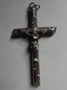 a silver cross on a white surface with a chain hanging from it's side