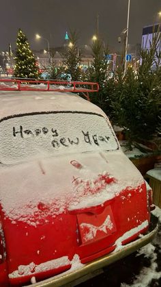 a red car covered in snow next to christmas trees