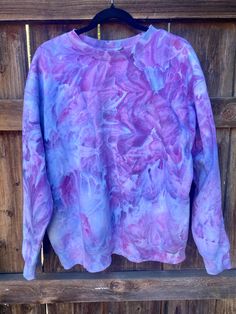 a purple and blue tie dyed sweatshirt hanging on a wooden fence with wood slats behind it