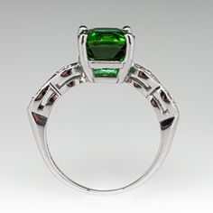 This balanced ring is centered with one (1) square cushion cut vivid green tourmaline set into a four-prong head. The shoulders of the ring are each accented with two (2) bead set round brilliant cut diamonds. The ring measures 8.2mm at the top, rises 7.1mm above the finger, tapering to 1.3mm wide and 0.7mm thick at the base of the shank. The ring is crafted in platinum and is currently a size 6. Classic Green Tourmaline Jewelry, Modern Green Jewelry With Accent Stones, Luxury Green Cushion Cut Jewelry, Classic Green Emerald Ring With Gemstone Accents, Formal Tourmaline Emerald Ring With Accent Stones, Green Radiant Cut Ring With Accent Stones, Green Radiant Cut Rings With Accent Stones, Radiant Cut Green Rings With Accent Stones, Green Square Cut Stone Jewelry