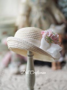 a white hat with flowers on it sitting on top of a wooden stand in front of a doll