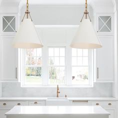 two lights hanging over a kitchen island in front of a white counter top and cabinets