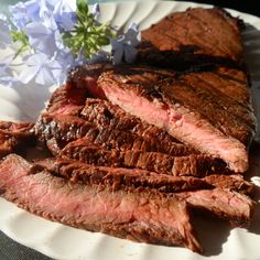 a white plate topped with sliced steak next to purple flowers and blue hydranges