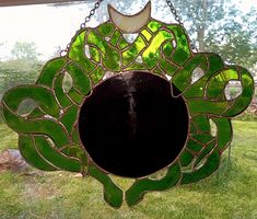 a green stained glass sun catcher hanging from a chain on the window sill outside