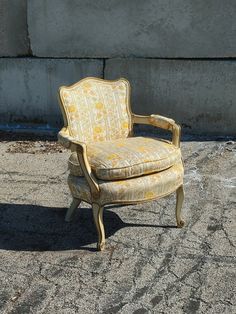 an old chair sitting in front of a concrete wall with no one around it on the ground