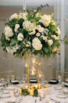 a tall vase filled with white flowers and greenery on top of a round table