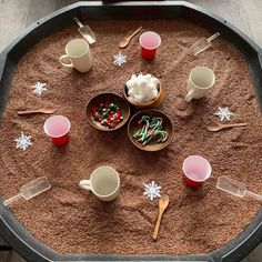 there are cups and spoons in the sand on the table with candy canes