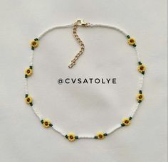 a white beaded bracelet with yellow flowers and green beads on the clasp is shown