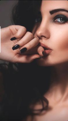 a woman with black nail polish holding her hand up to her face and posing for the camera