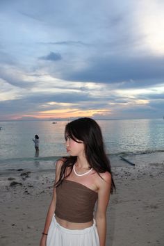 a young woman standing on top of a sandy beach next to the ocean at sunset