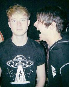 two young men standing next to each other in front of a black background with an alien t - shirt on