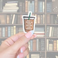 a hand holding up a sticker with a coffee cup on it in front of bookshelves