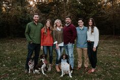 a group of people standing next to each other in the grass with two dogs on leashes