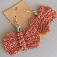 two pairs of tasseled earrings on top of a piece of brown paper next to a tag