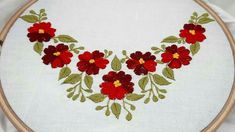 a close up of a embroidery on a white cloth with red flowers and green leaves