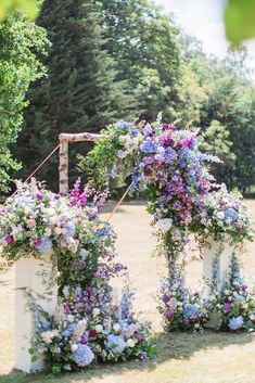 three white pedestals with purple and blue flowers on them in front of some trees