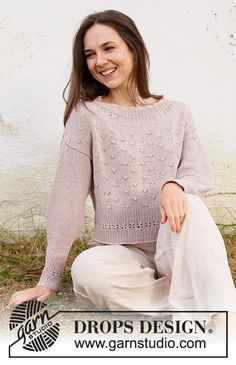 a woman sitting on the ground wearing a sweater