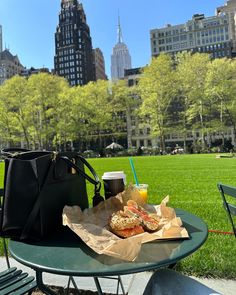 a picnic table with food and drink on it in the middle of a city park