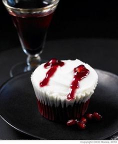 a cupcake with white frosting and cranberry sauce on a black plate