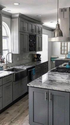 a large kitchen with gray cabinets and marble counter tops is pictured in this image, there are two pendant lights hanging over the island