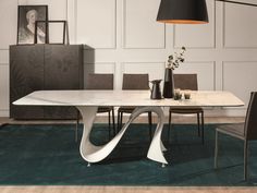 a modern dining room table with chairs and vases on the top, in front of a white paneled wall